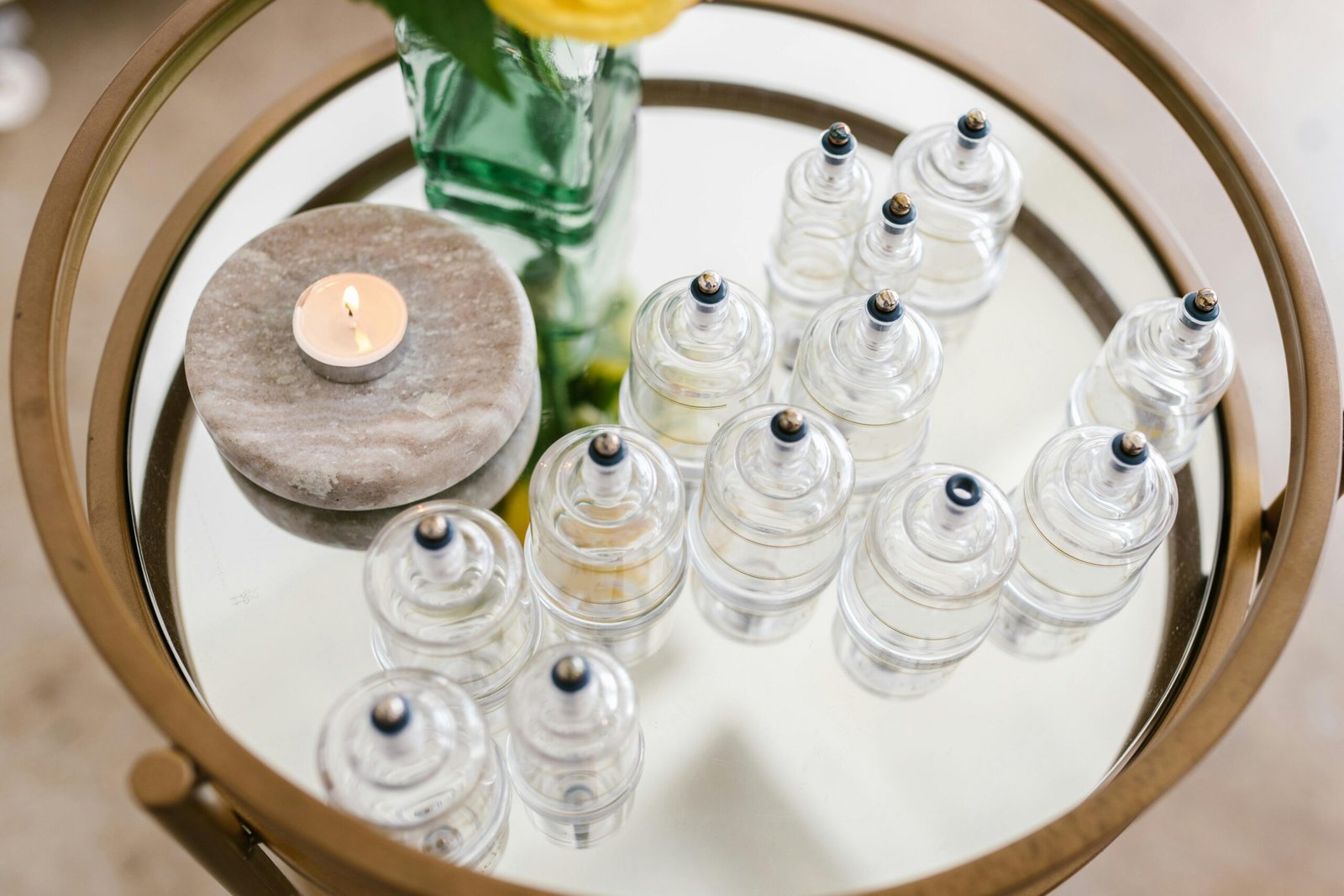 A stylish arrangement of glass cupping jars on a mirrored table with a candle and flowers, ideal for spa settings.