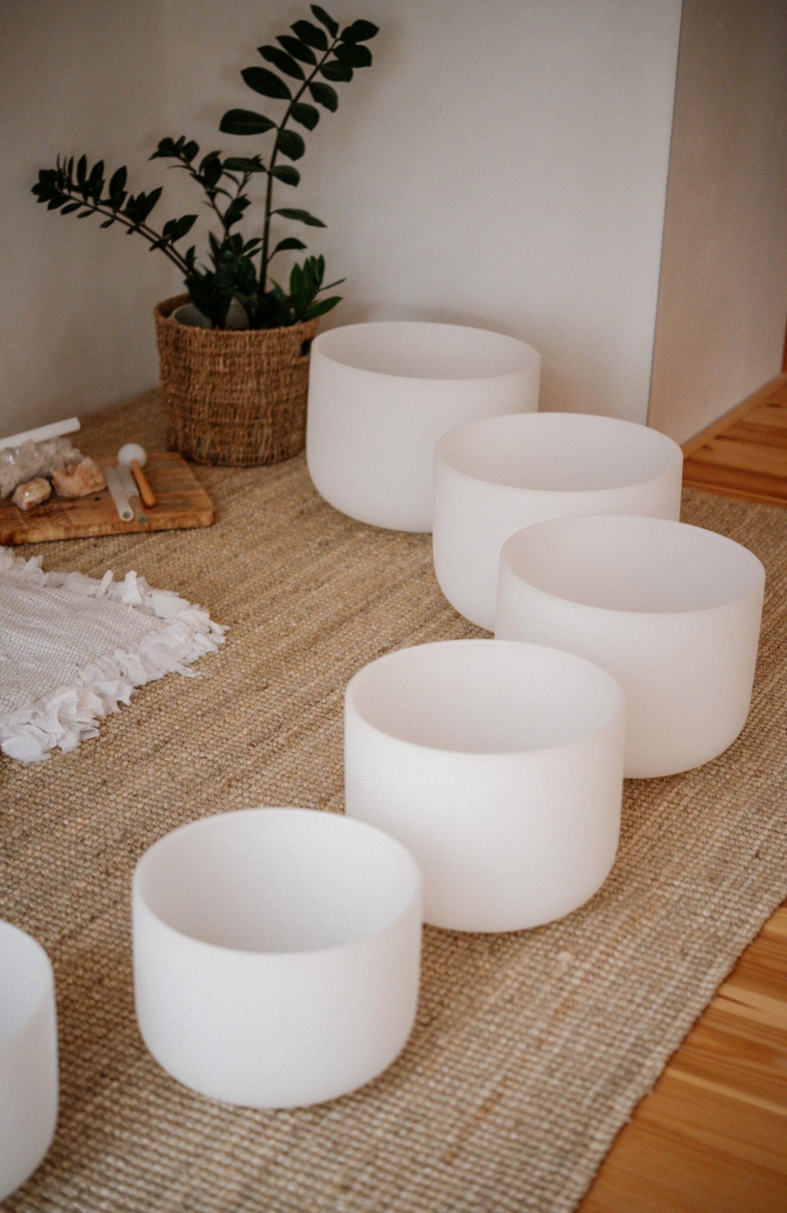 Crystal singing bowls arranged on a jute rug by a potted plant, creating a serene ambiance.